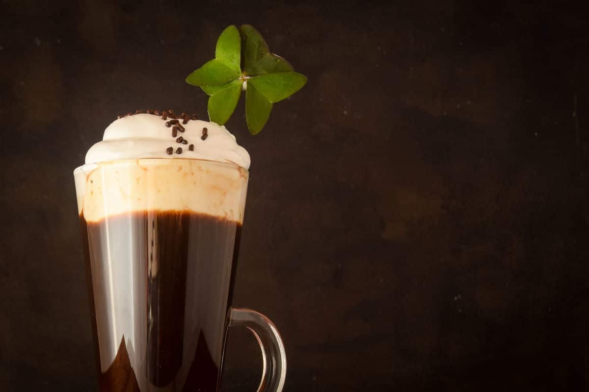 Irish Coffee with a four-leaf clover on brown background.