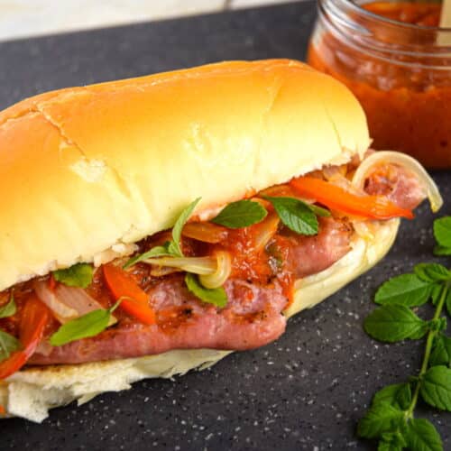 Italian sausage sandwich with fresh oregano and a jar of pepper sauce on the side.