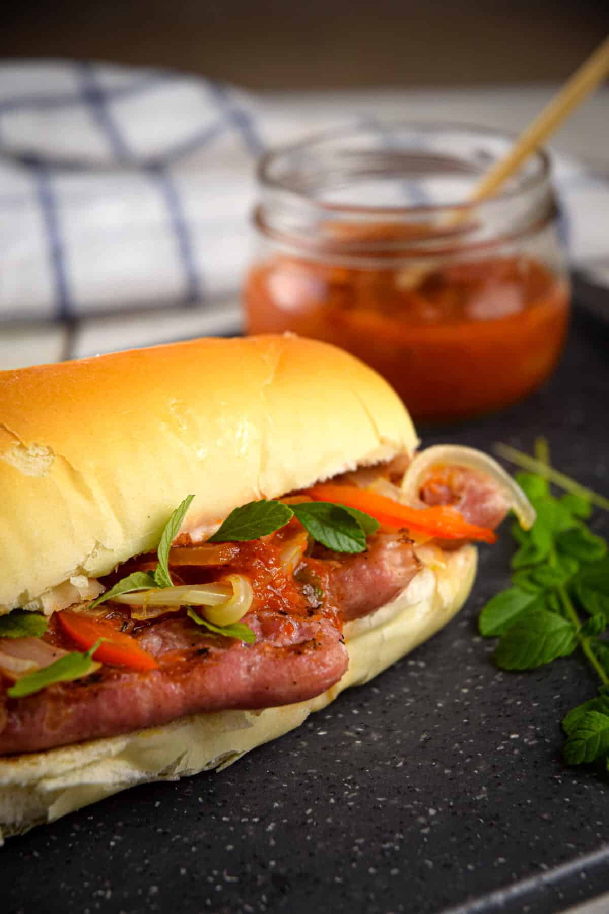 Italian sausage sandwich with fresh oregano and a jar of pepper sauce.