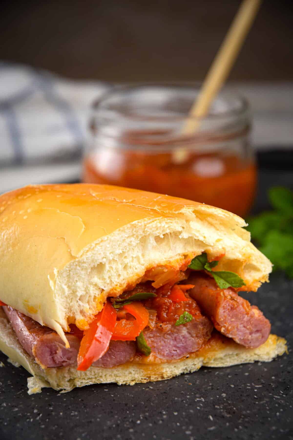 Italian sausage sandwich with a jar of pepper sauce in the background.