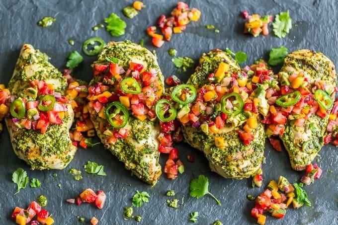 Grilled chicken breasts with salsa and jalapenos side by side on stone.