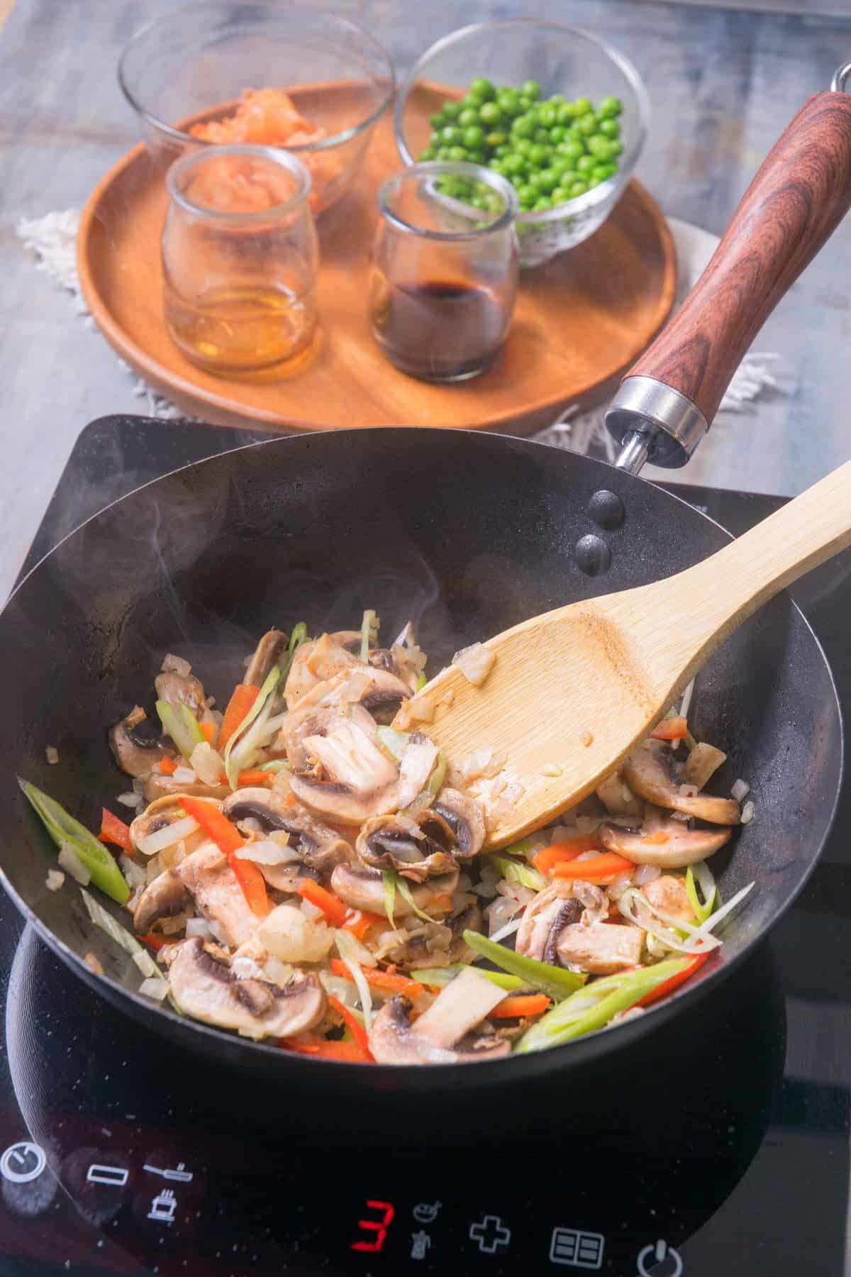 Stir fried veggies in pan with wooden spoon.