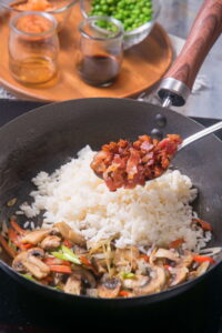 Rice, vegetables and bacon in frying pan.