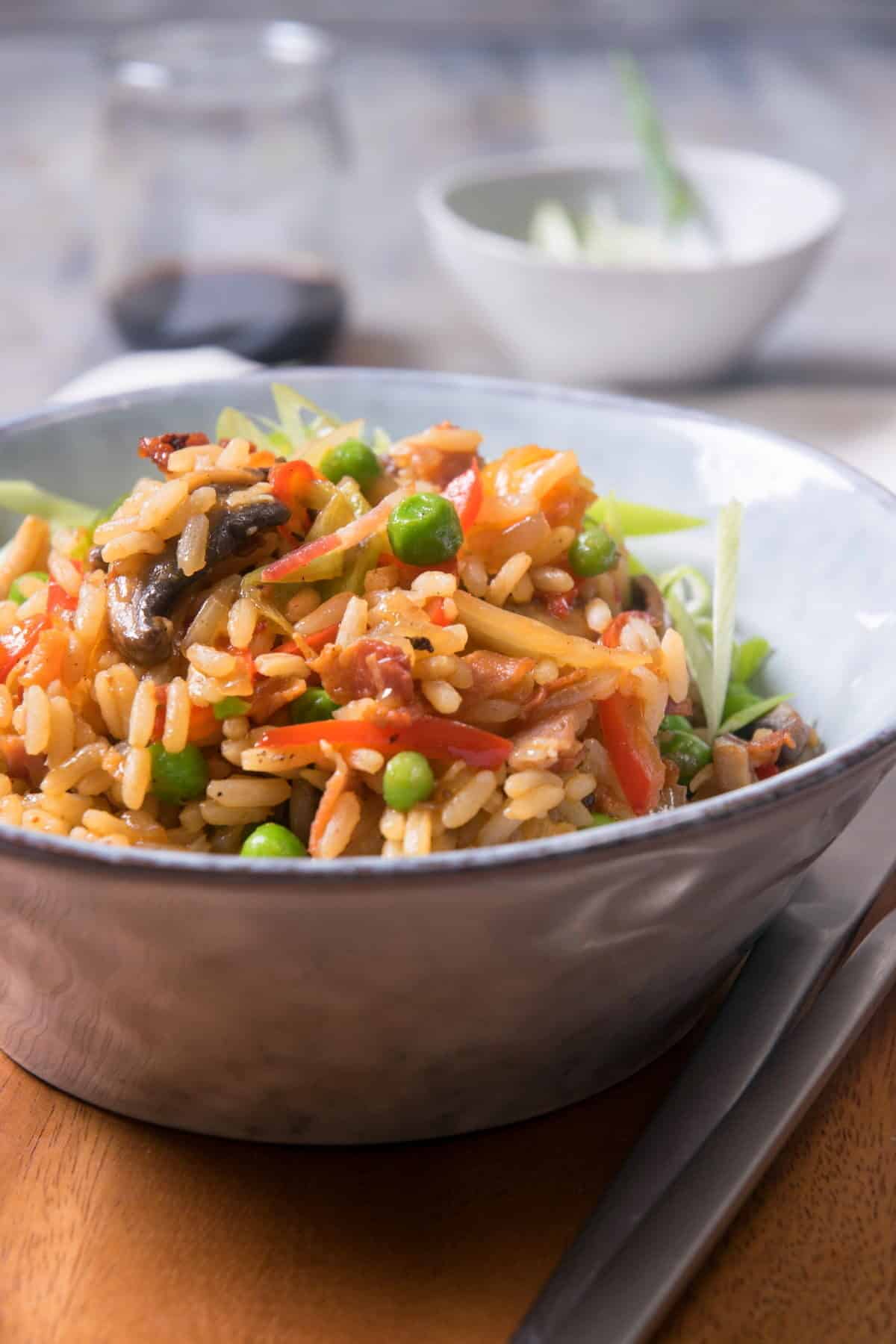 Kimchi bacon fried rice in bowl, with fork and knife on the side.