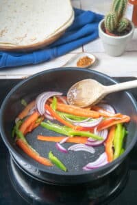 Sliced peppers and onions in a frying pan.