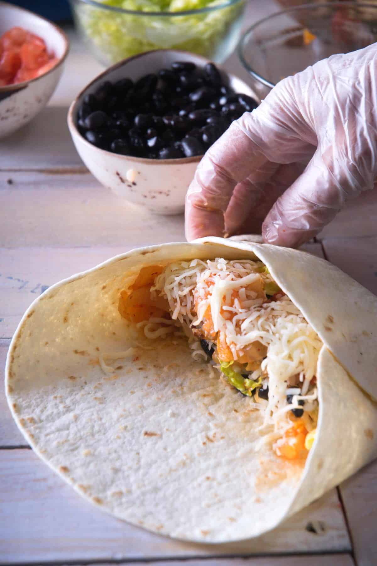 Tortilla with burrito ingredients being wrapped up.