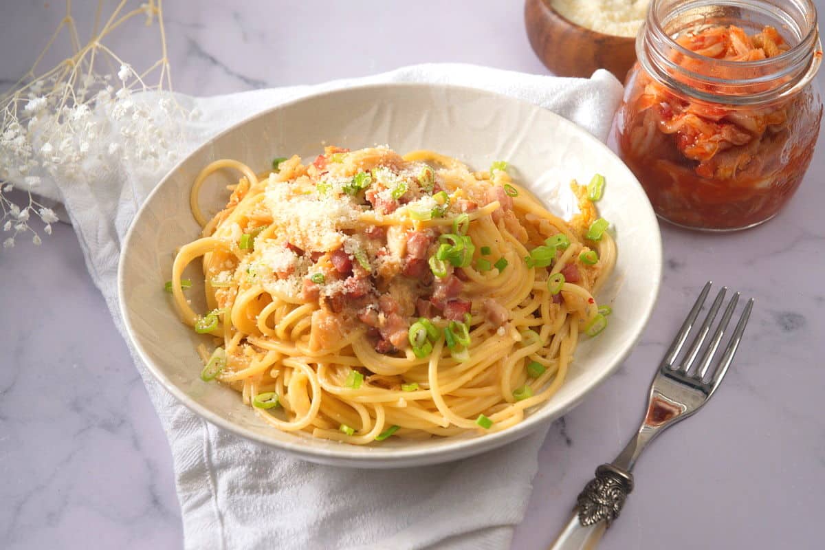 Kimchi carbonara in a white bowl with kimchi on the side.