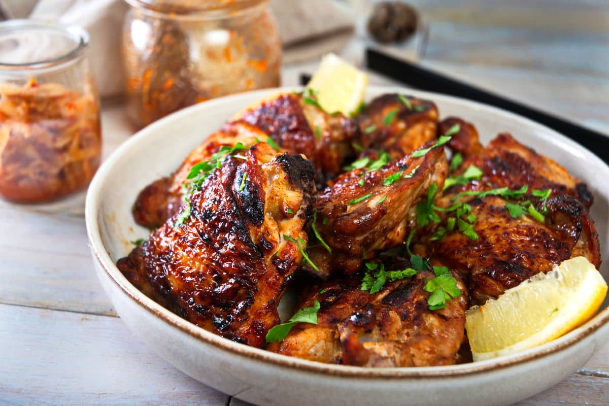 Kimchi chicken thighs in light dish with lemon wedges on the side.