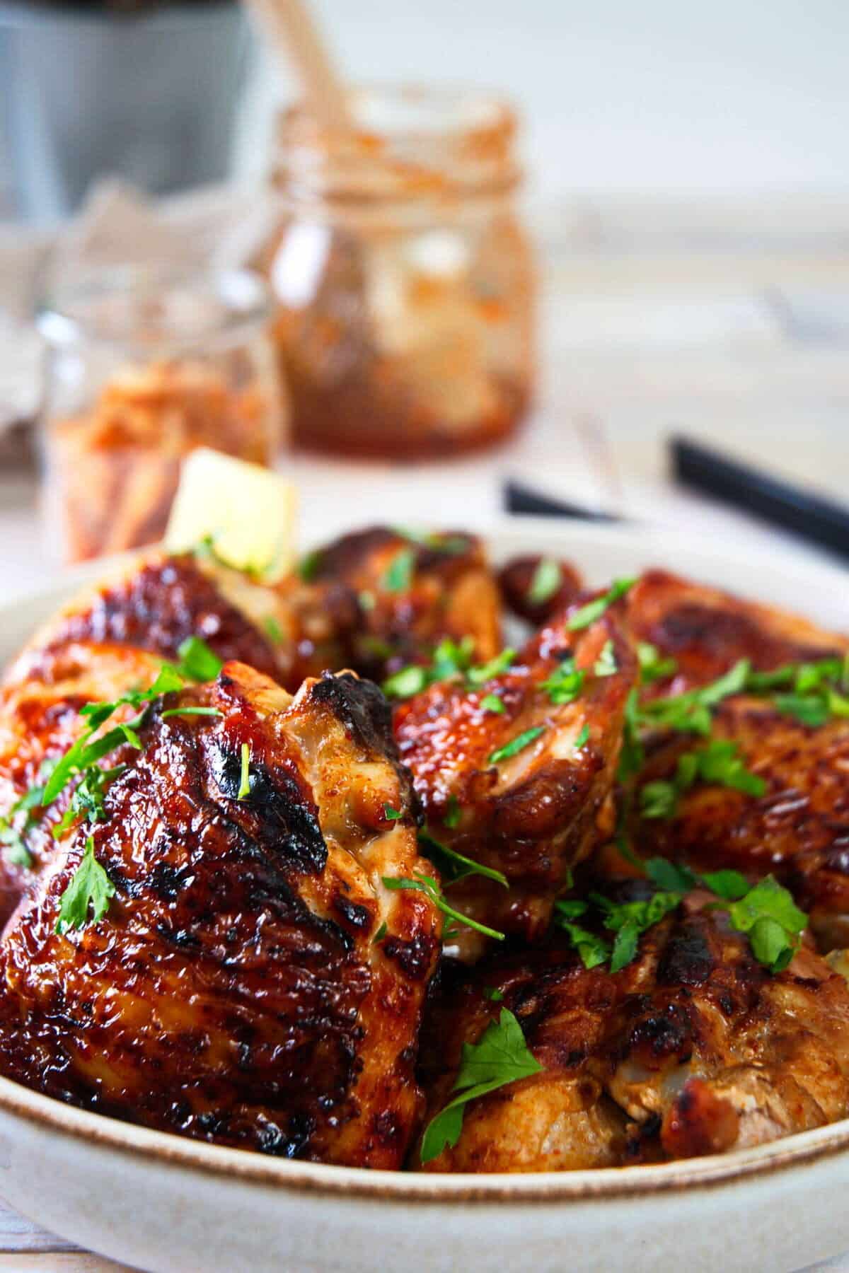 Kimchi chicken thighs in light dish with chopped parsley.