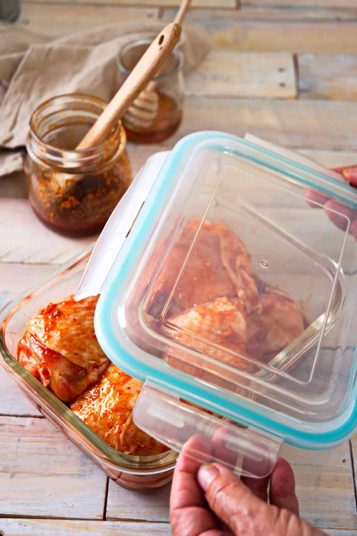 Chicken thighs in a marinade in glass container, wooden background.