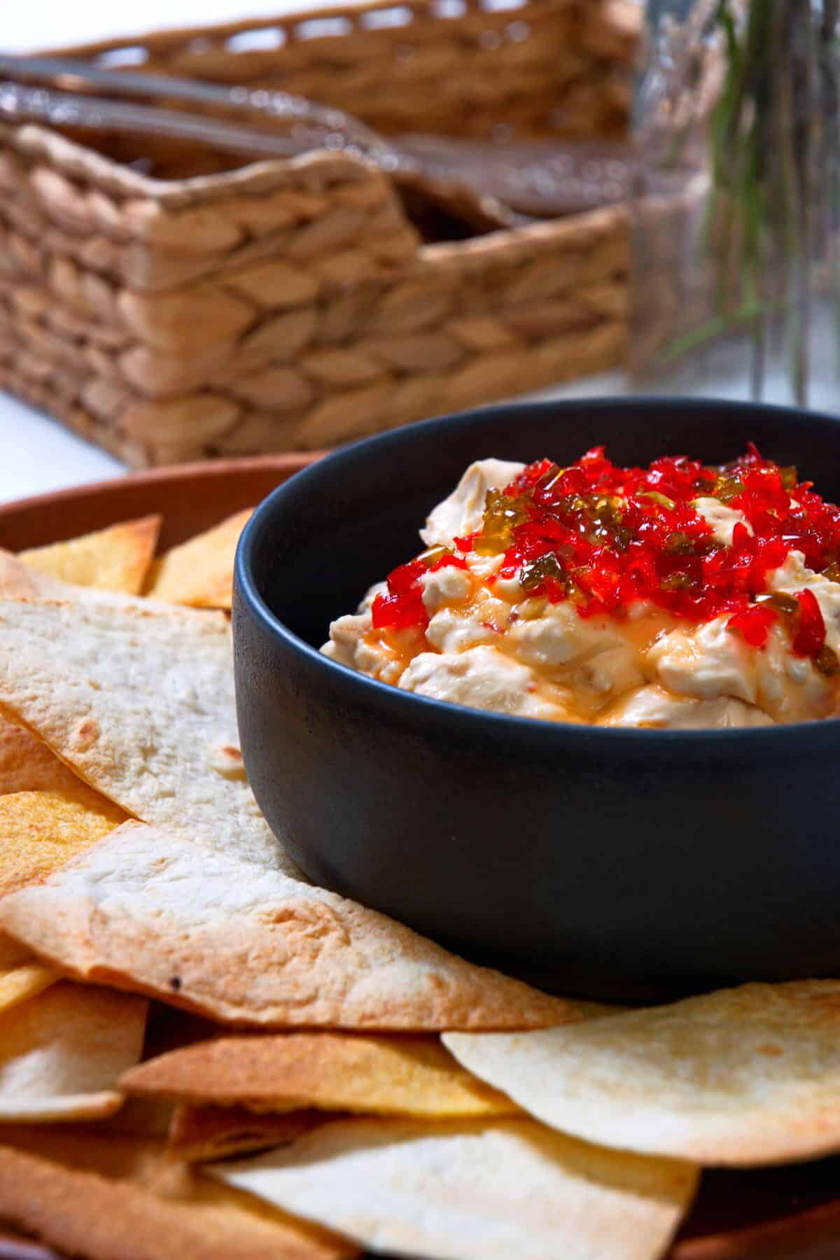Kimchi cream cheese spread in a small black bowl, surrounded by tortilla chips.