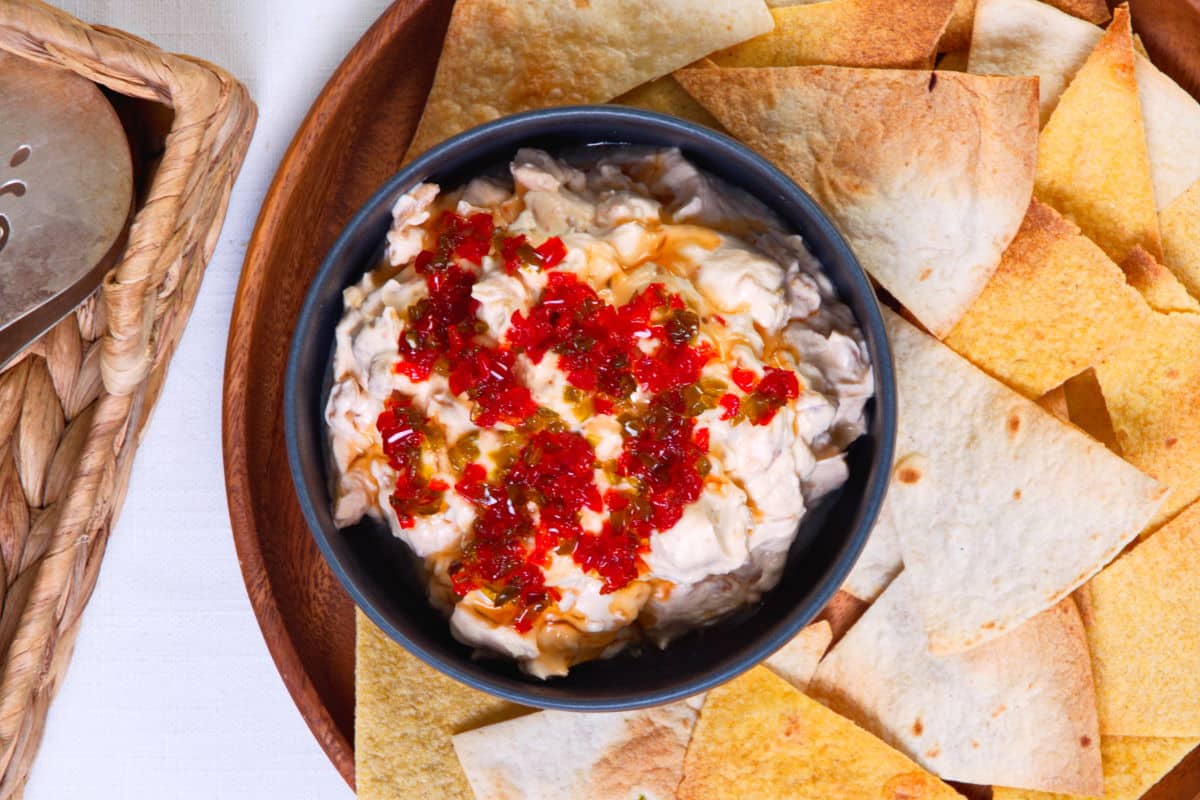 Kimchi cream cheese spread in a small black bowl, surrounded by tortilla chips.