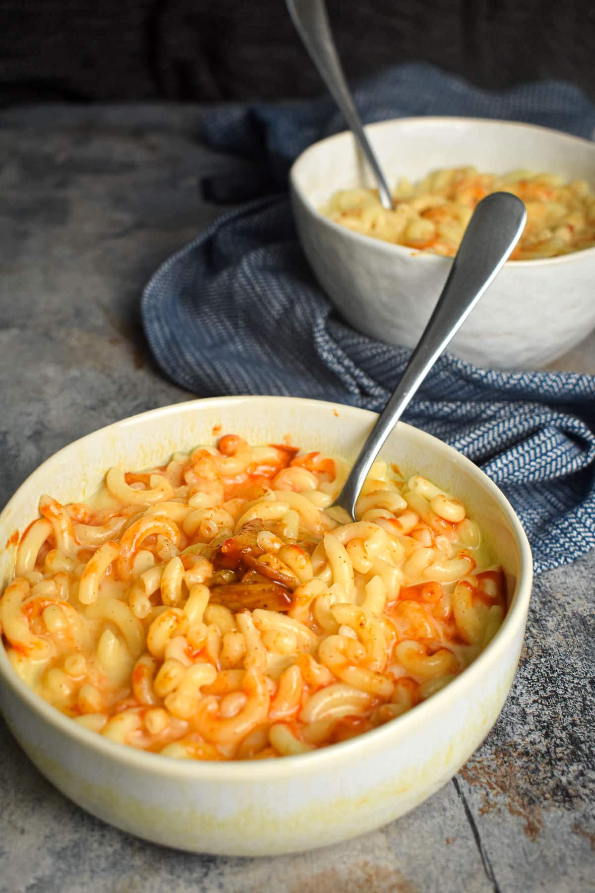 Kimchi mac and cheese in bowls with spoons on blue-grey background.
