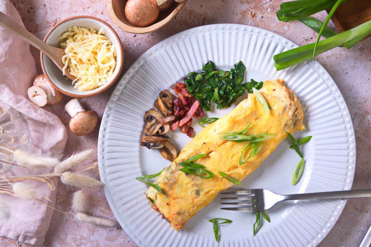 Top view of kimchi omelette on white plate with sliced scallions, grated cheese and mushrooms on the side.