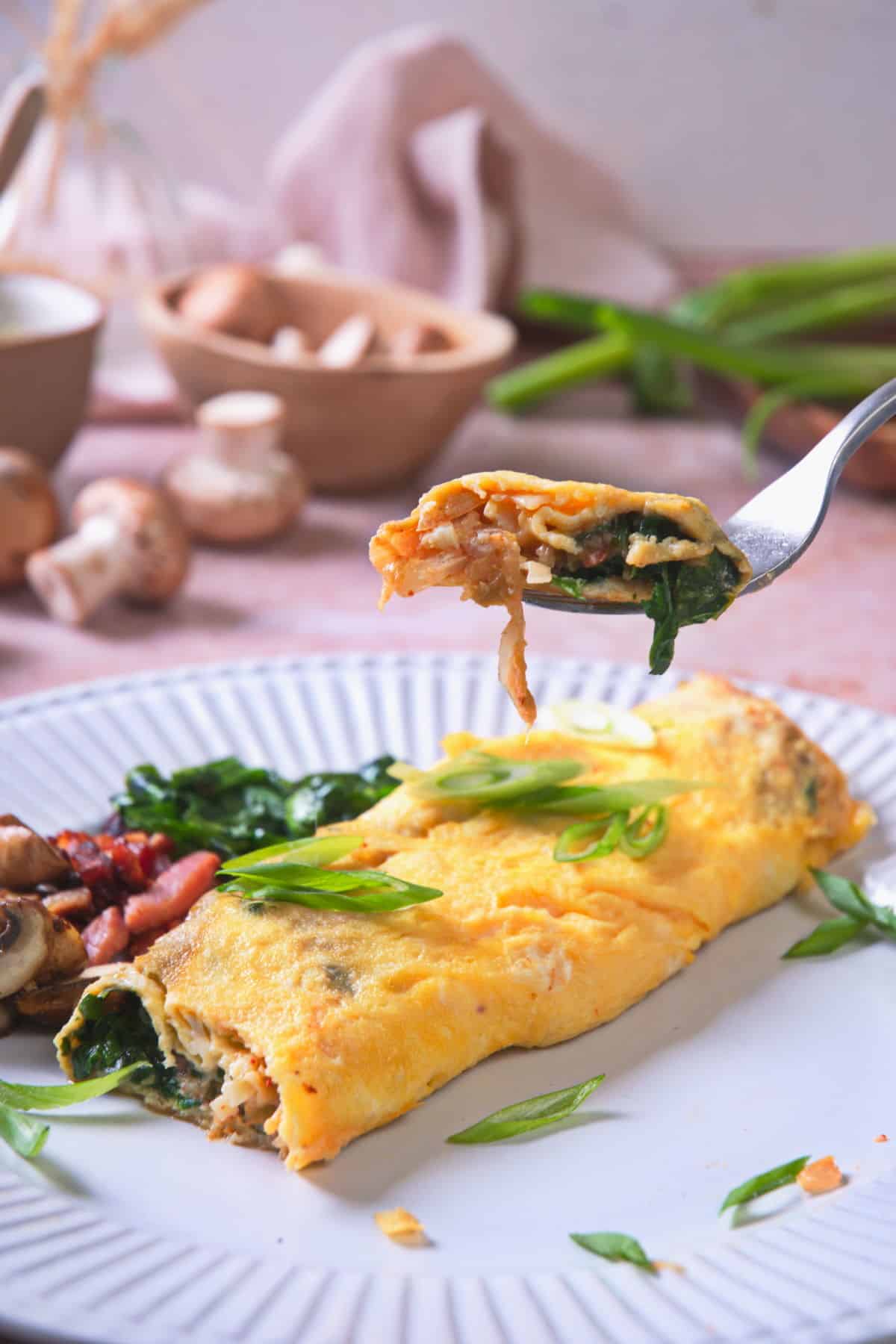 Kimchi omelette on white plate with sliced scallions and a fork.