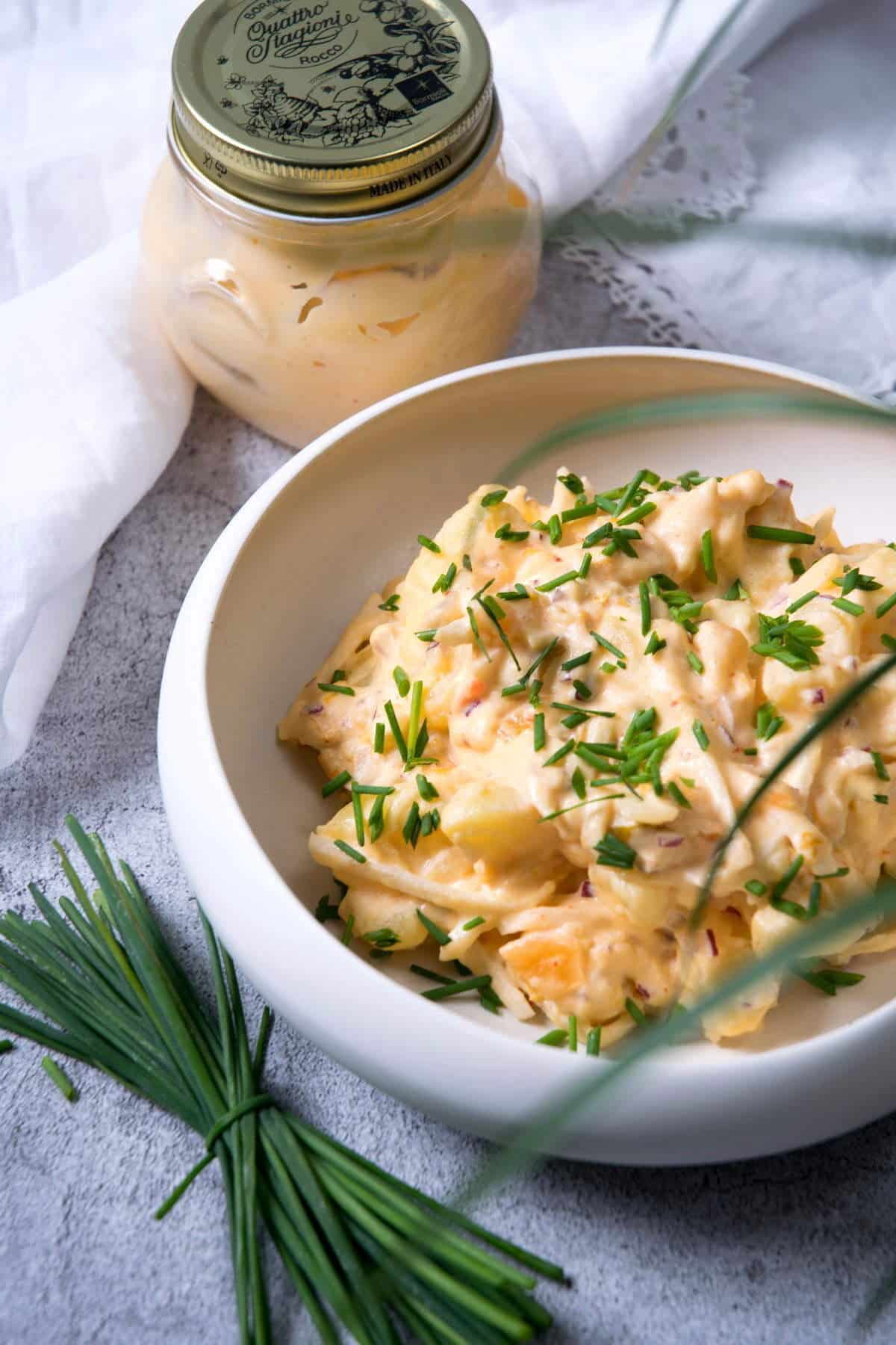 Kimchi potato salad in white bowl, kimchi mayo and chives on the side.