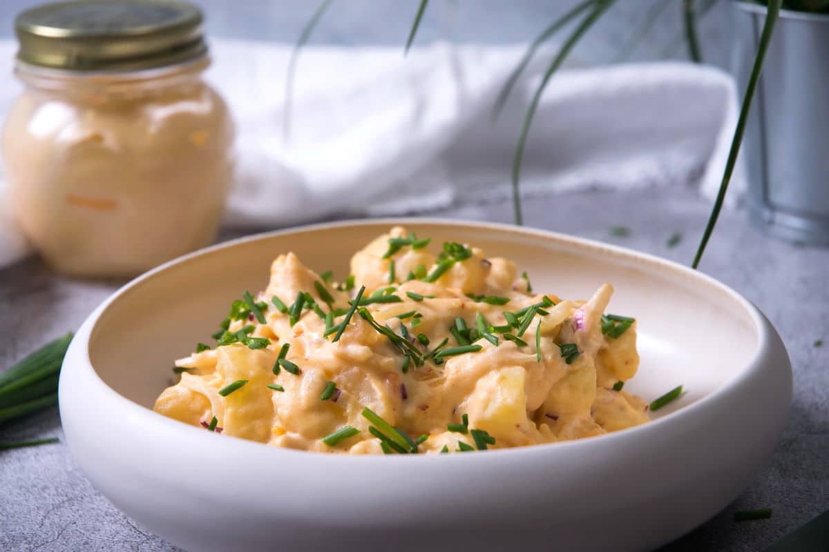 Kimchi potato salad in white bowl, kimchi mayo in the background.