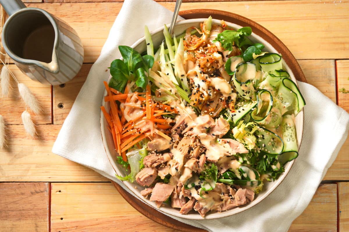 Kimchi tuna salad in bowl on wooden background, dressing on the side.