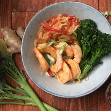 Kimchi and shrimp stir fry over rice in a bowl on wooden background, overhead shot.