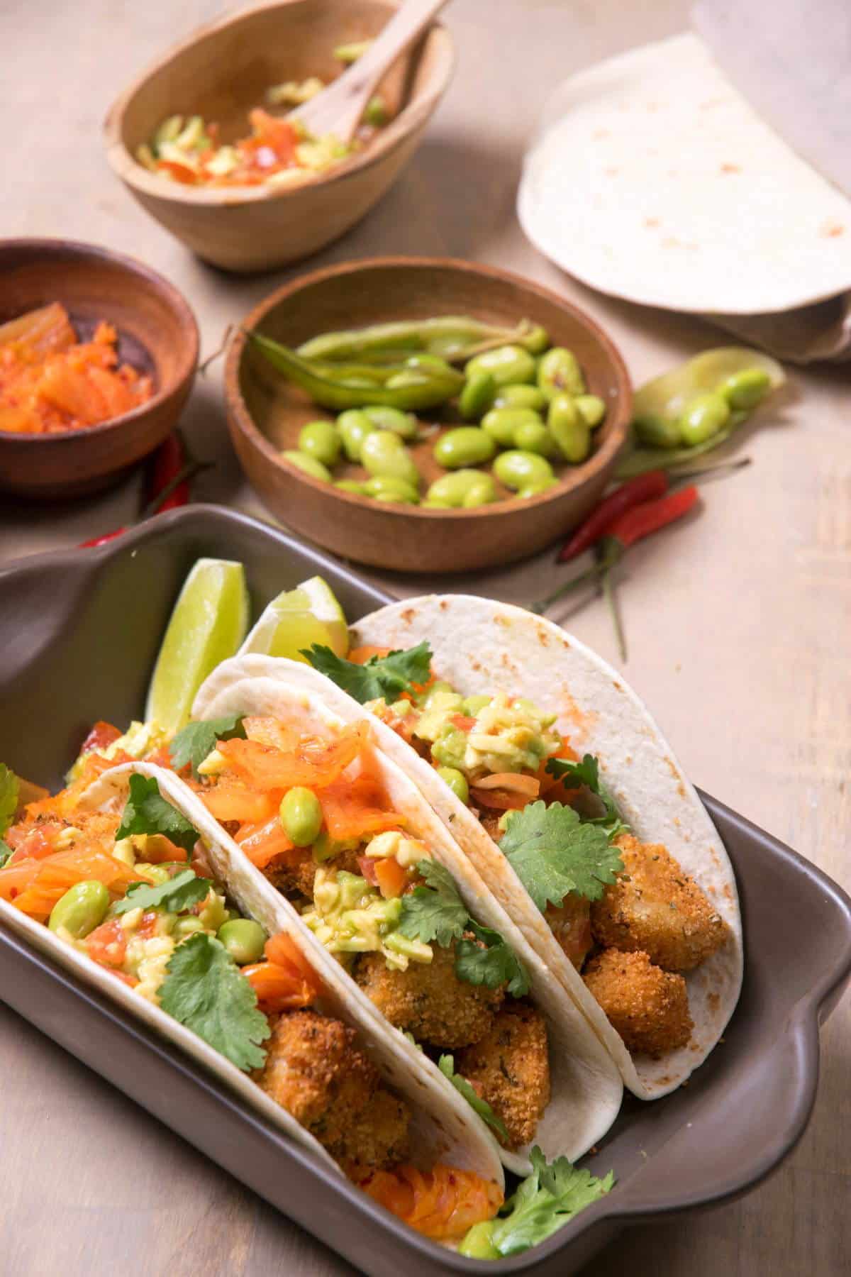 Kimchi and cod tacos stacked in a brown serving dish.