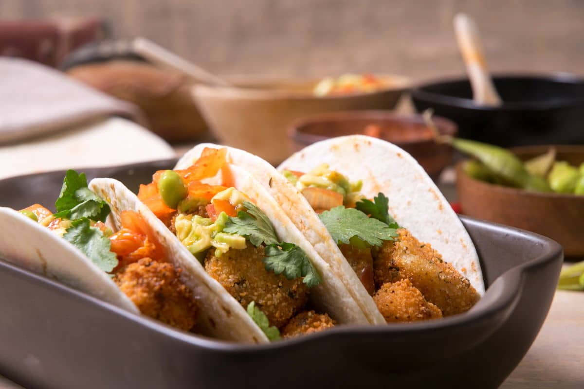 Kimchi and cod soft tacos standing up in a brown dish.