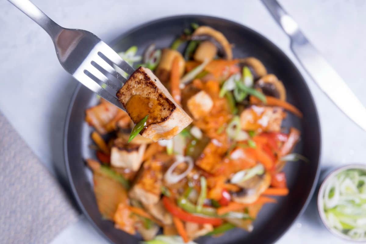 Kimchi tofu stir fry on black dish with a fork.