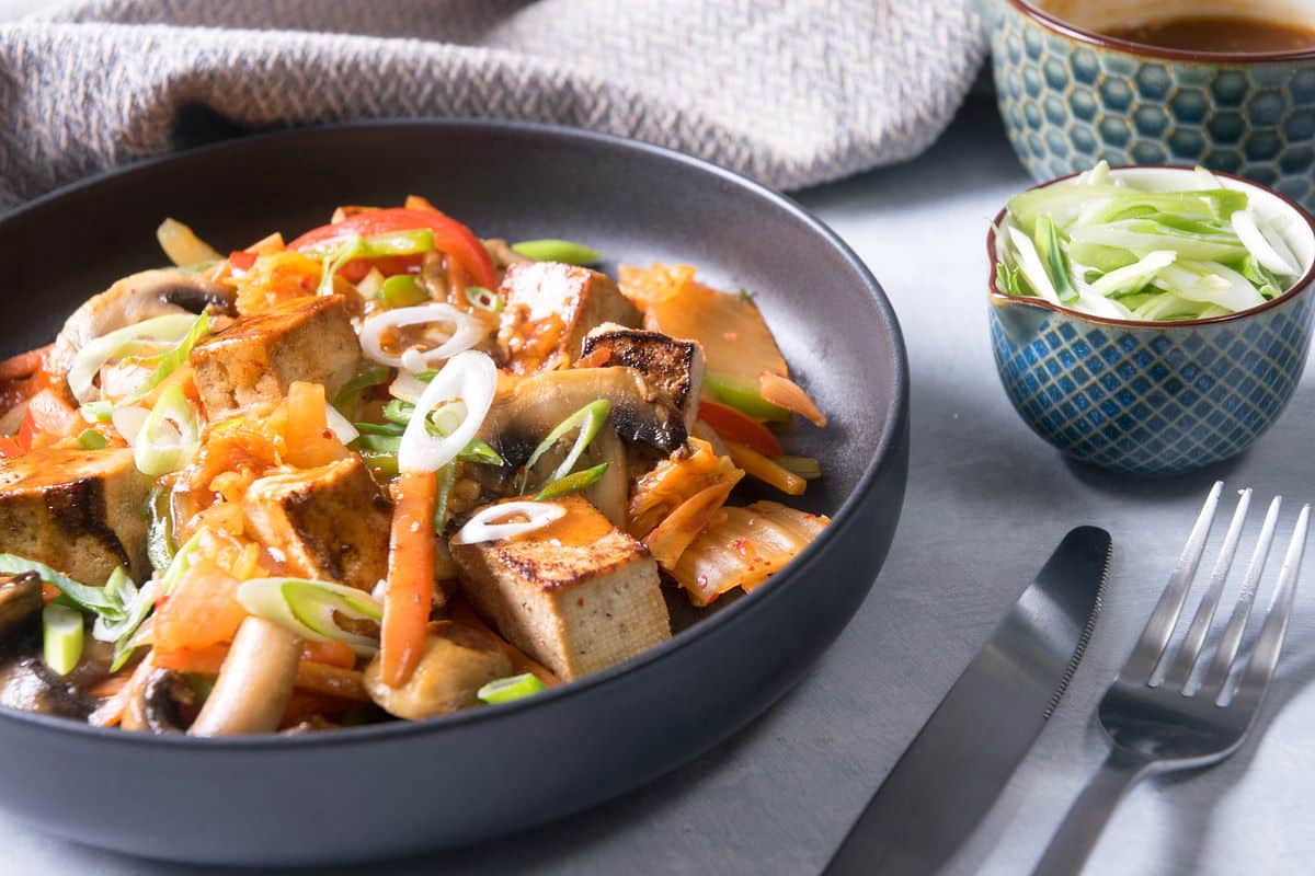 Kimchi tofu stir fry on black dish, fork and knife on the side.