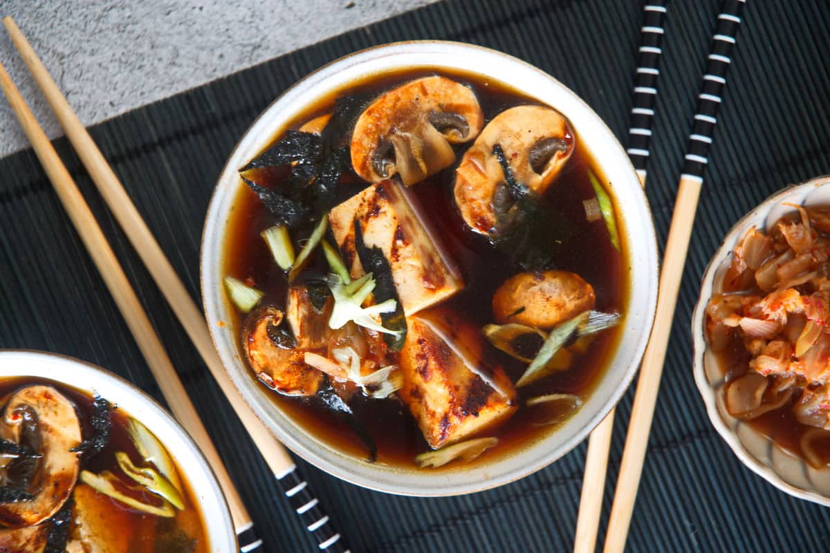 Top view of kimchi tofu soup in a bowl on black mat and chopsticks on the side.