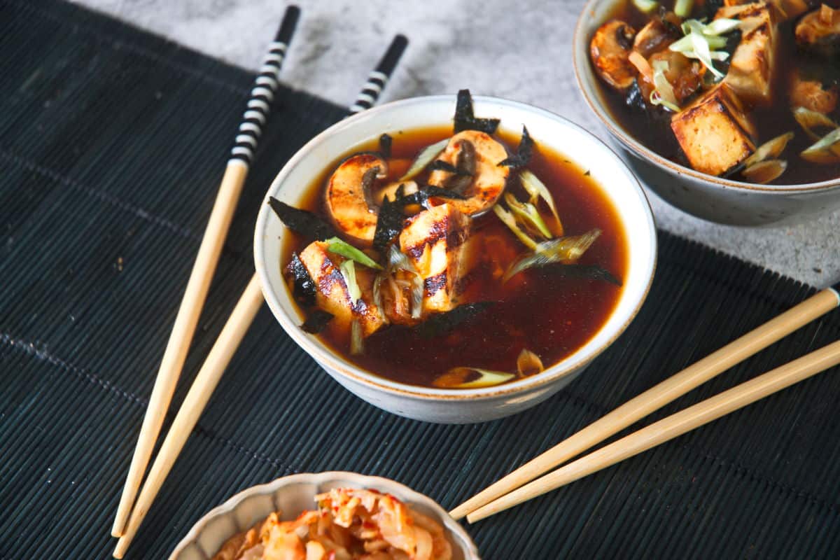 Kimchi tofu soup in a bowl with black placemat and chopsticks on the side.