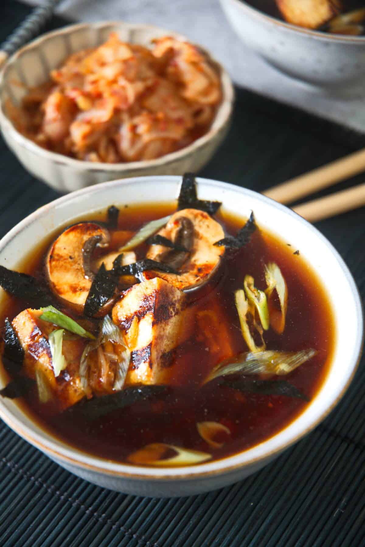 Kimchi tofu soup in a bowl with kimchi in the background.