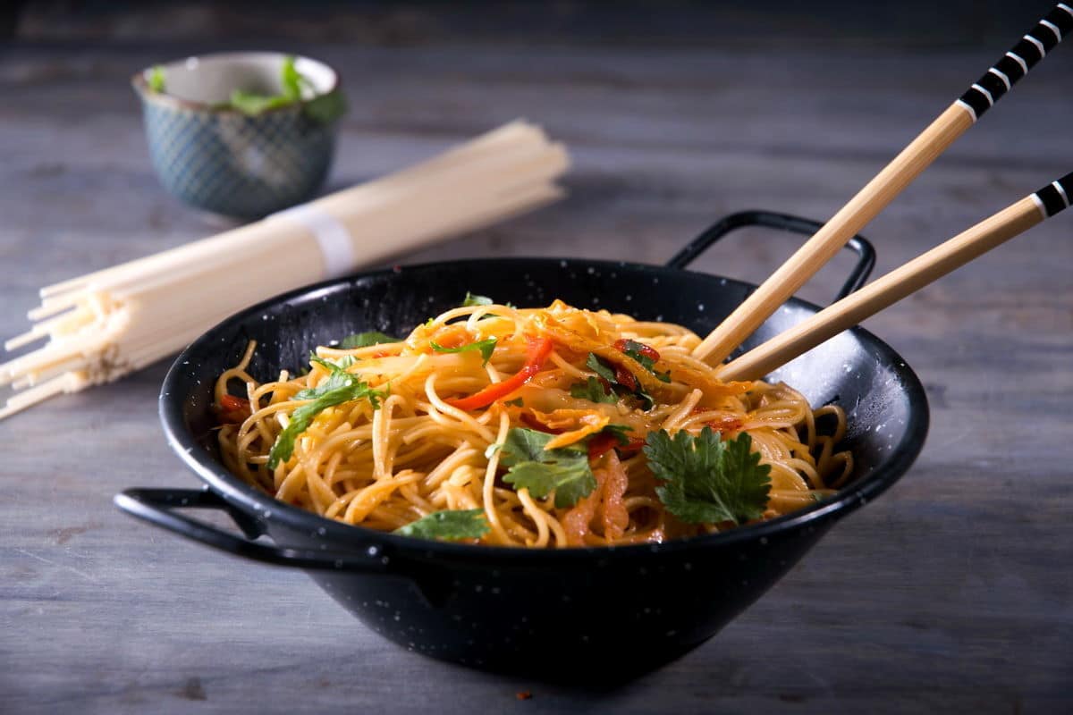 Kimchi udon noodle stir fry in a black bowl with chop sticks.