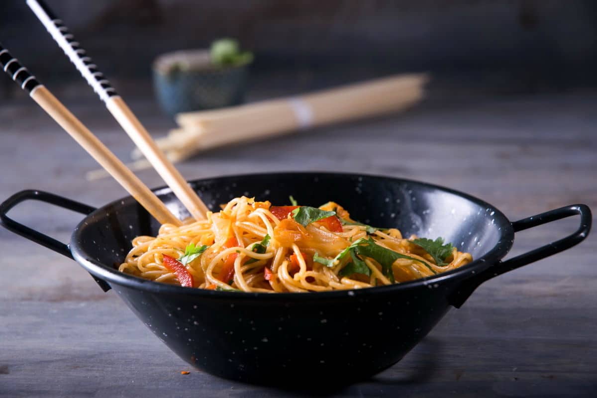 Kimchi udon noodle stir fry in a black bowl with chop sticks.