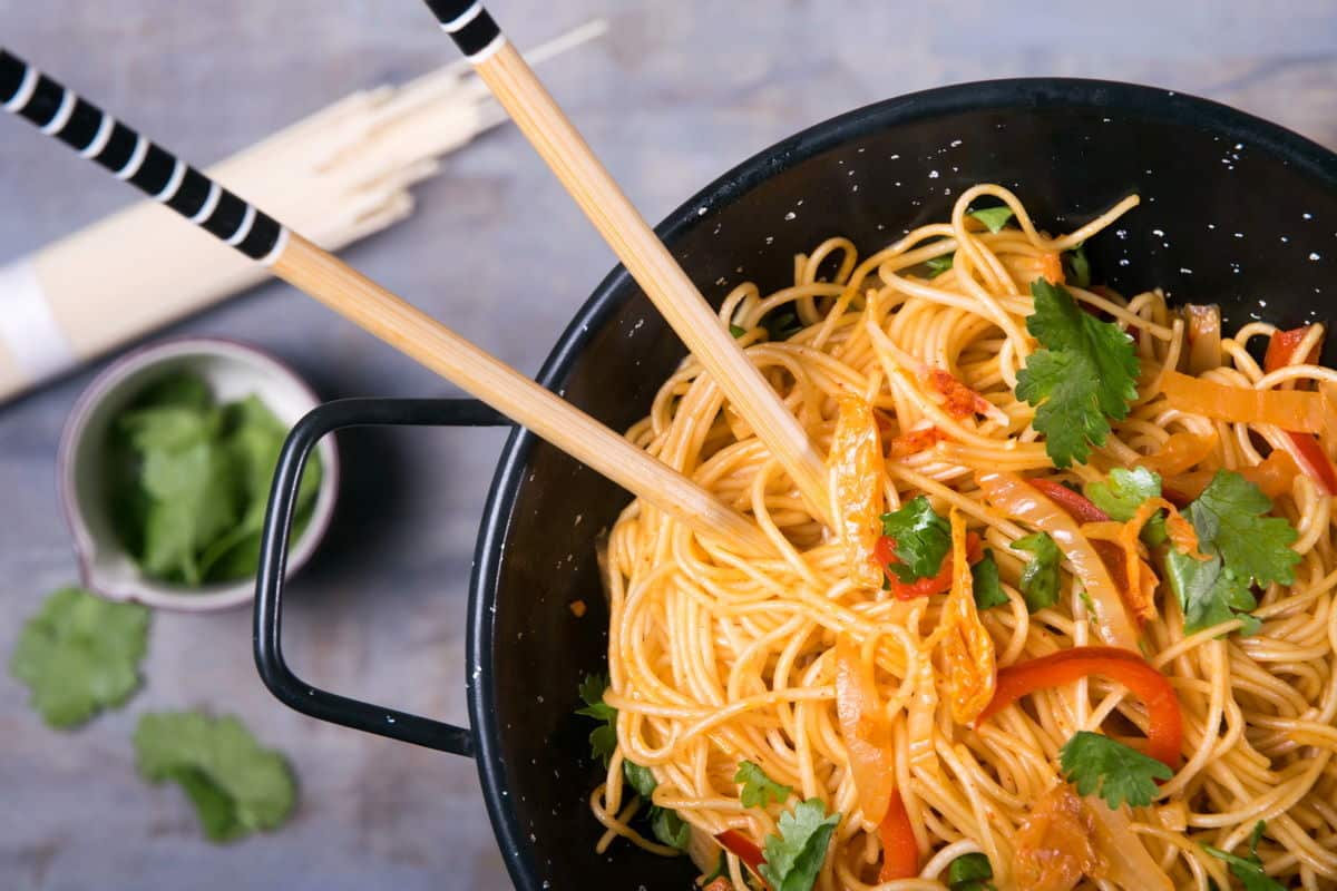 Kimchi udon noodle stir fry in a black bowl with chop sticks.