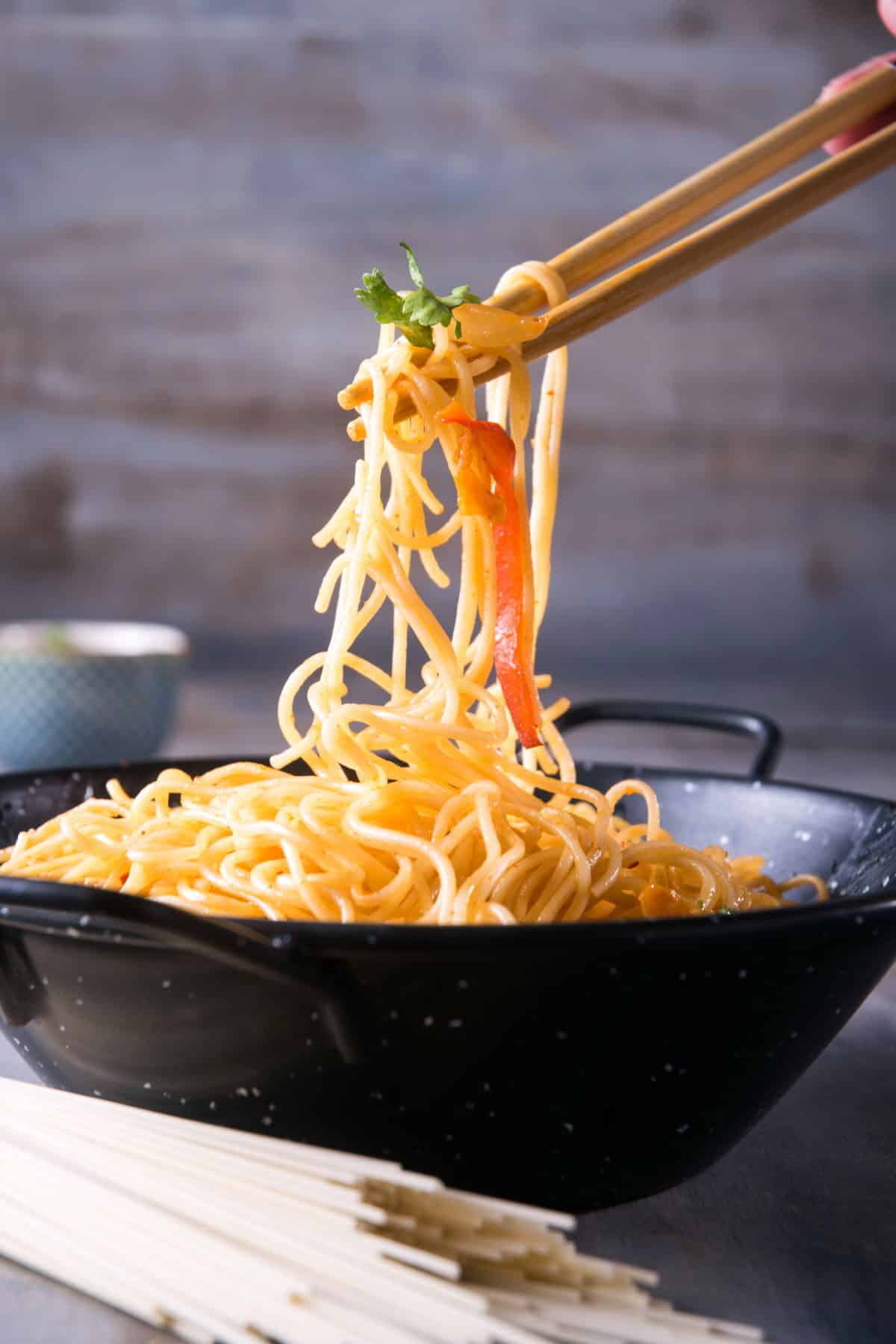 Kimchi udon noodle stir fry in a black bowl with chop sticks and dry udon on the side.