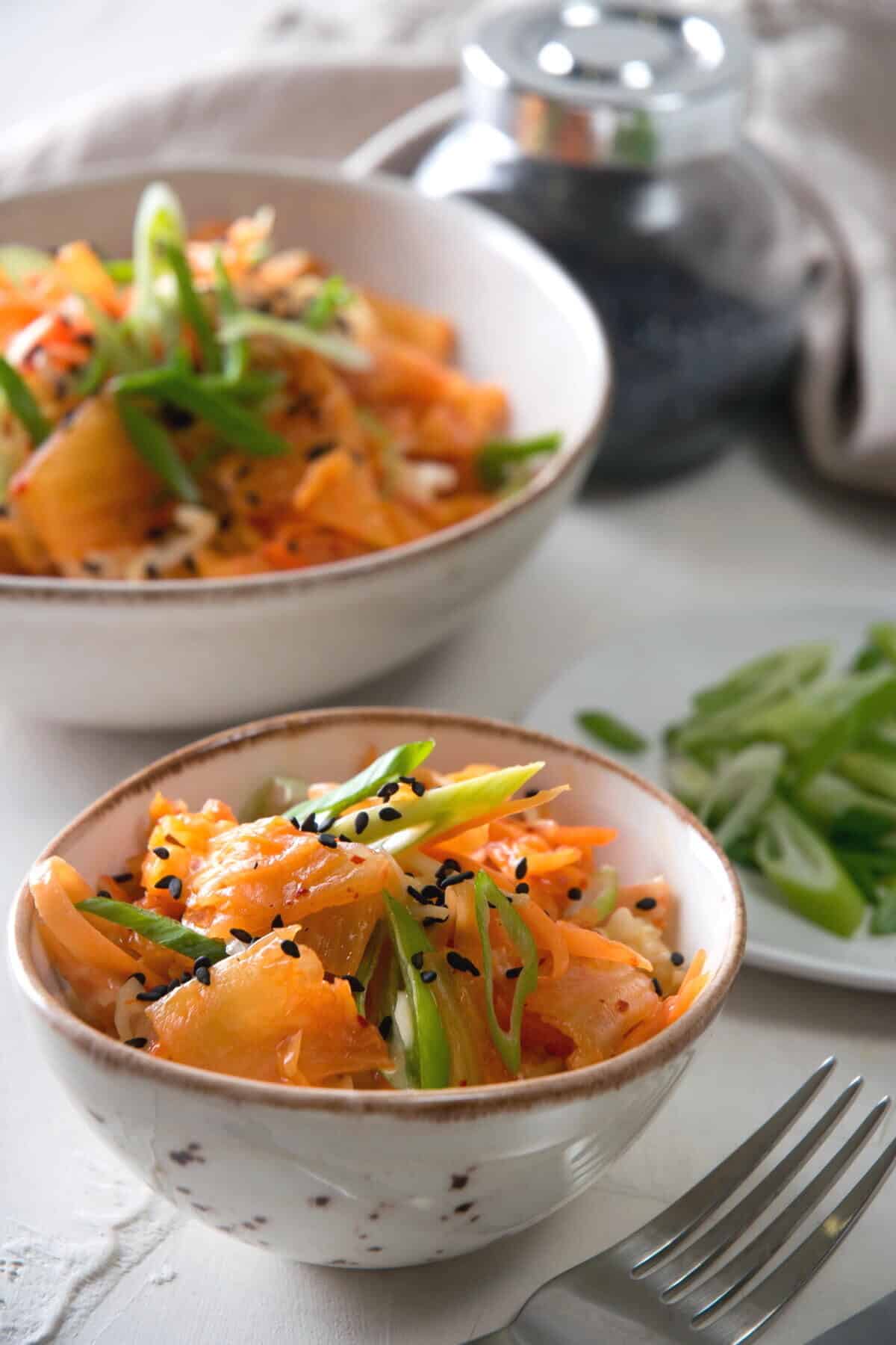 2 bowls of kimchi slaw with sliced scallions and black sesame seeds.