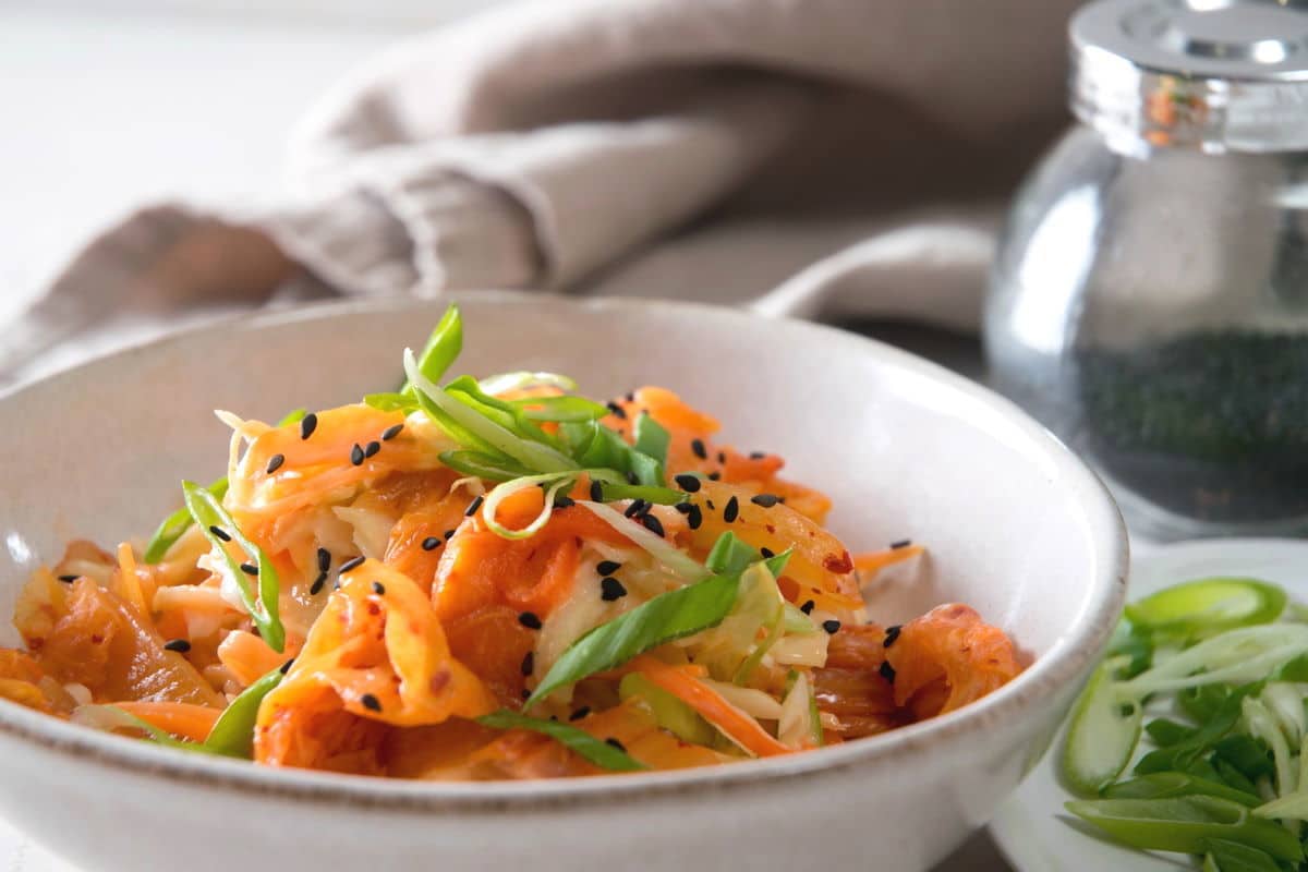 Kimchi slaw in a bowl with sliced scallions and black sesame seeds.
