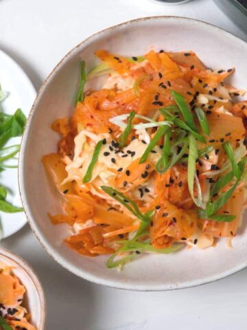Kimchi slaw in a bowl with sliced scallions and black sesame seeds.