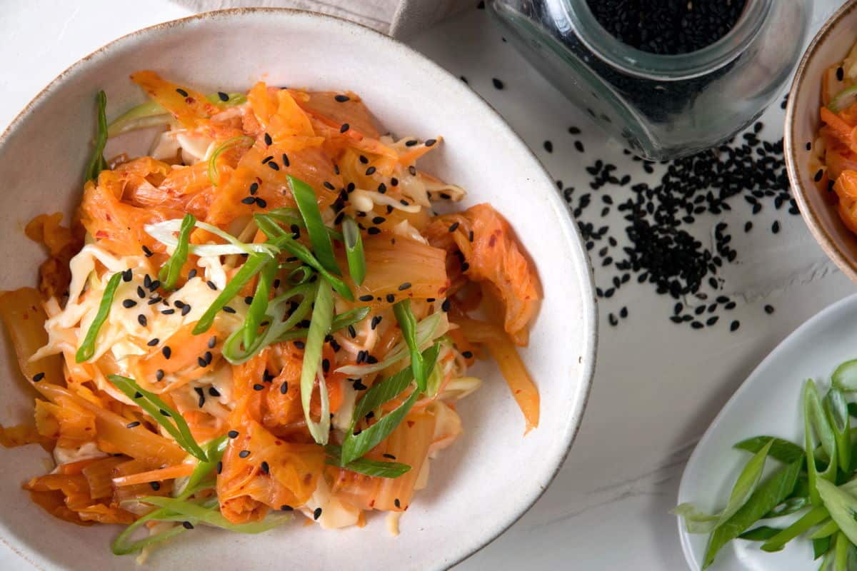 Kimchi slaw in a bowl with sliced scallions and black sesame seeds.