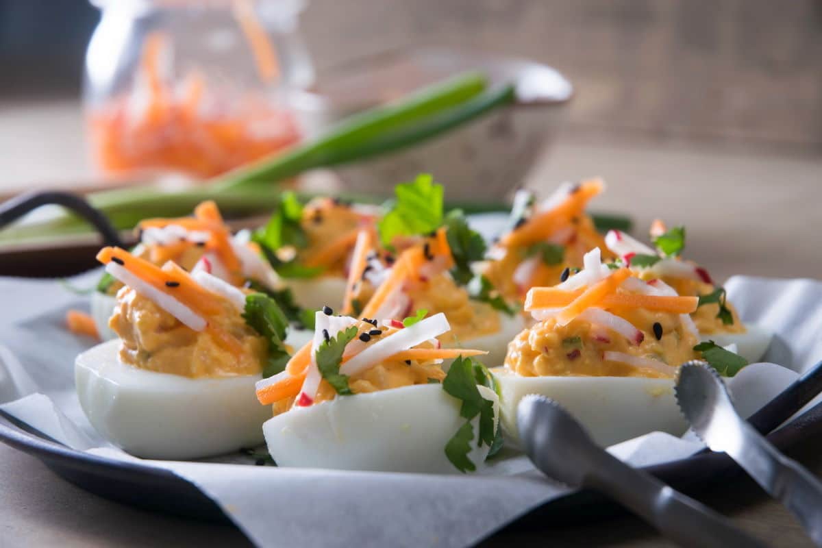 Kimchi deviled eggs on a plate with sliced green onion and sesame seed garnish.