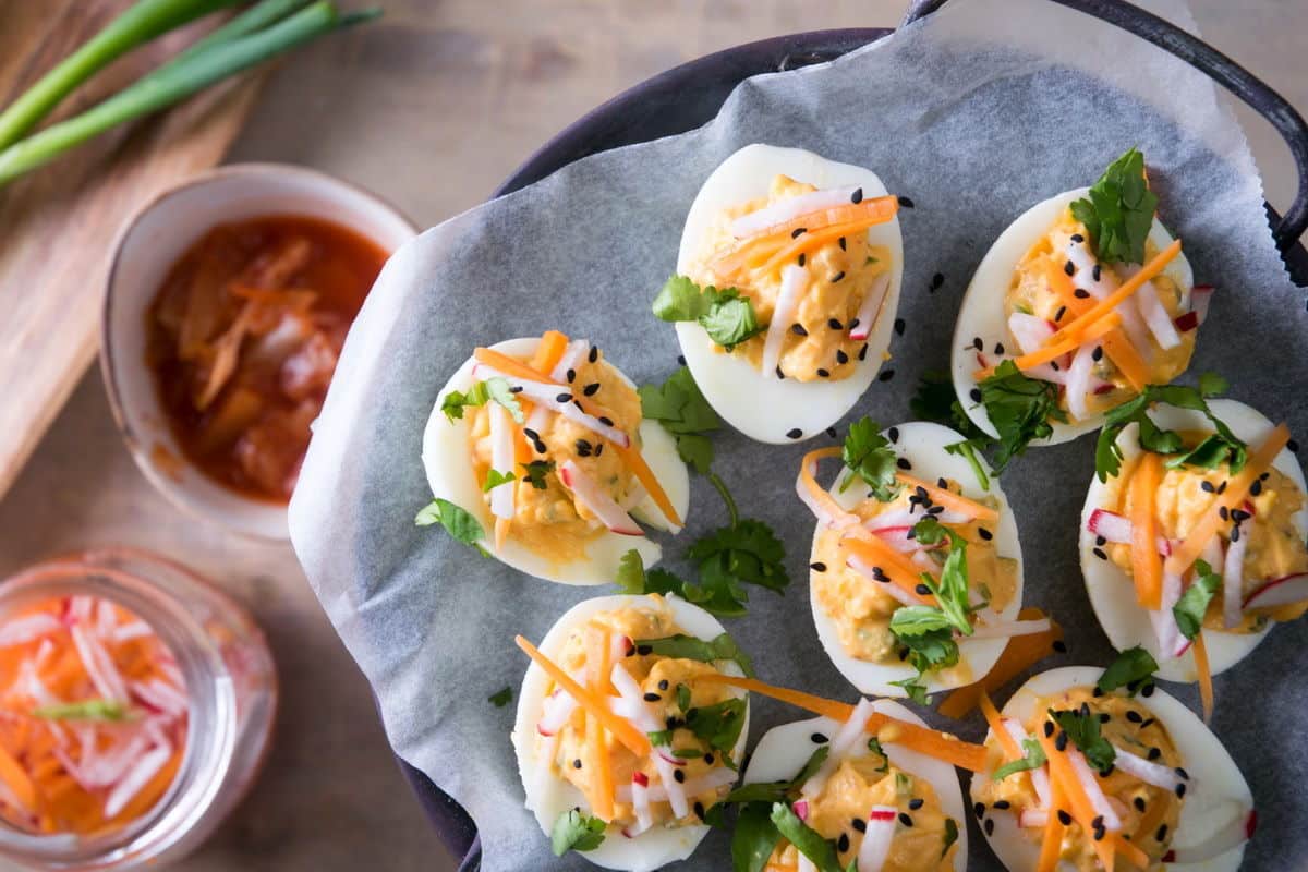 Kimchi deviled eggs on a plate with sliced green onion and sesame seed garnish, top view.