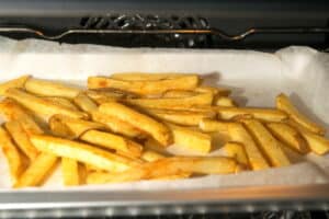 Fries in the oven on a baking sheet lined with parchment paper.