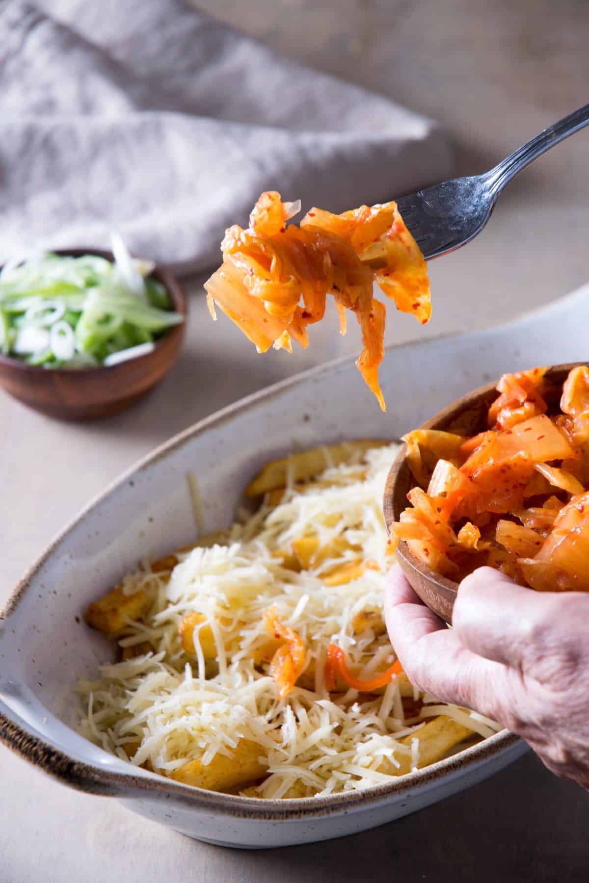 Baked fries with kimchi and shredded cheese in a casserole dish.
