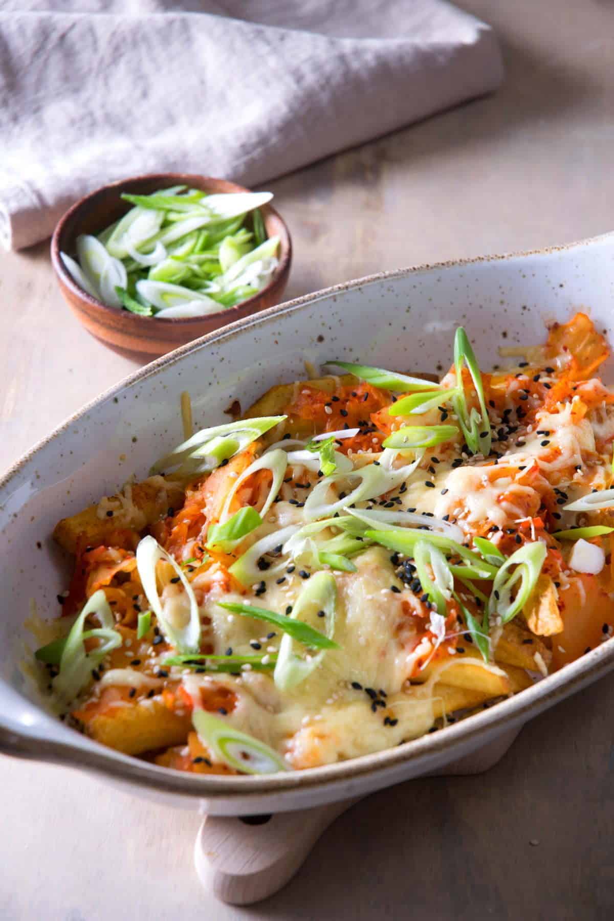 Fries with kimchi and cheese in a casserole dish. Sliced scallions on the side.