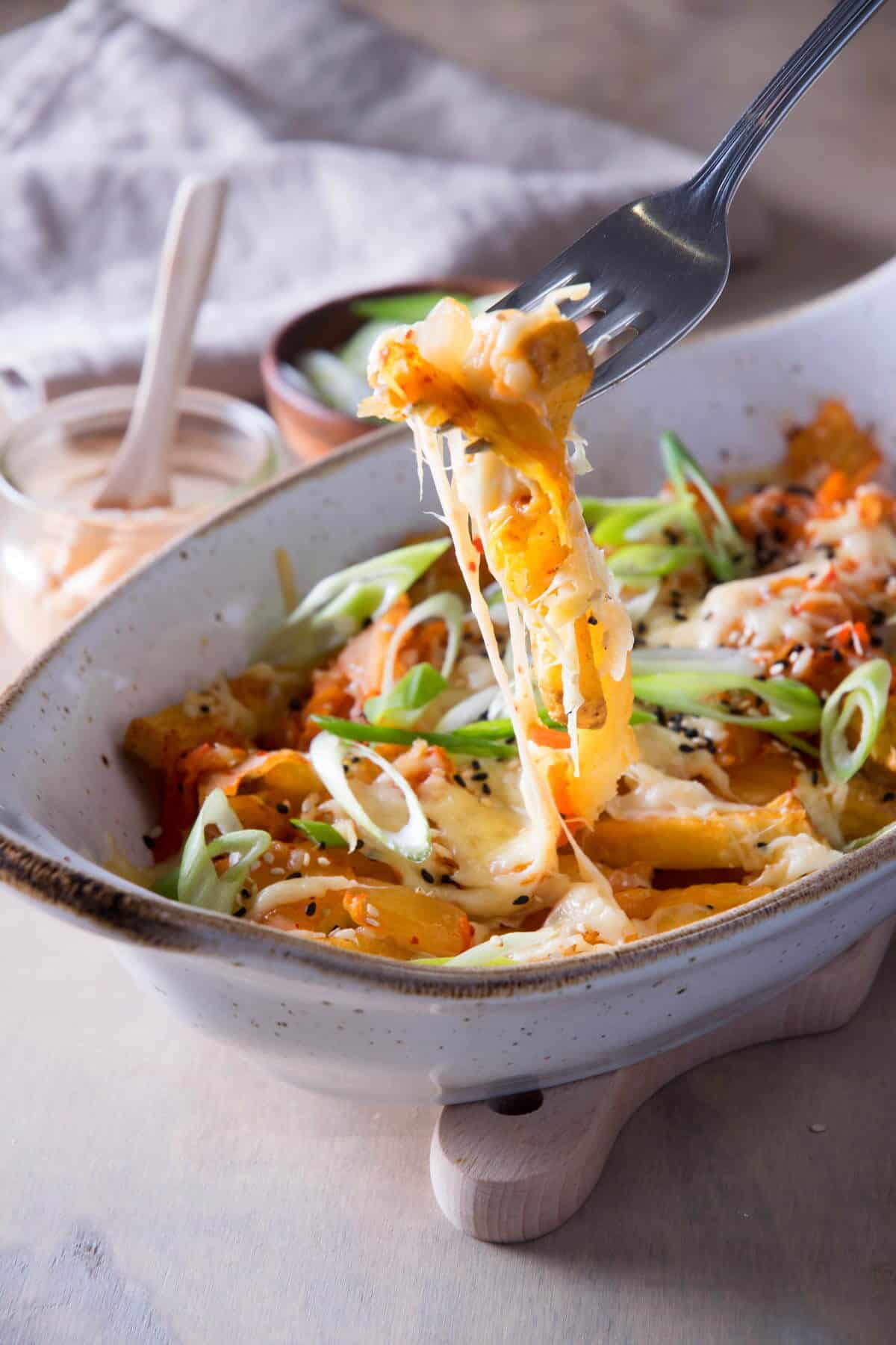 Fries with kimchi and cheese in a casserole dish with a fork.