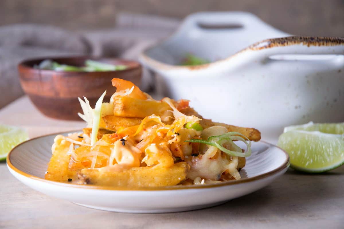 Fries with kimchi on a small plate. Lime wedges on the side.