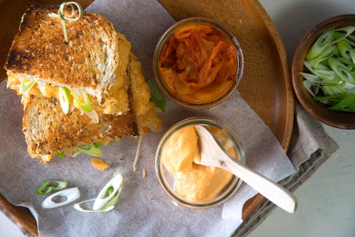 Kimchi grilled cheese sandwiches on a brown plate with kimchi, spicy mayo and green onions on the side.