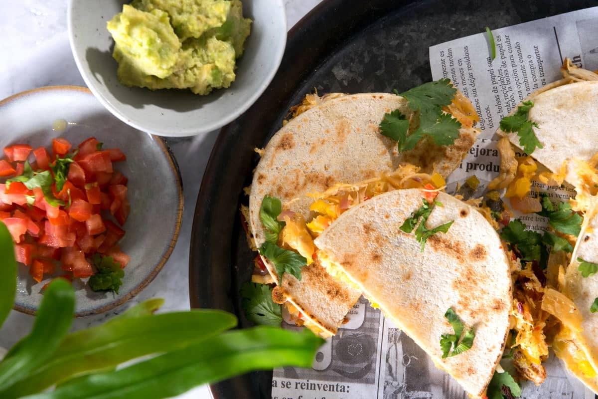 Kimchi quesadillas on dark plate with avocado and diced tomatoes on the side.