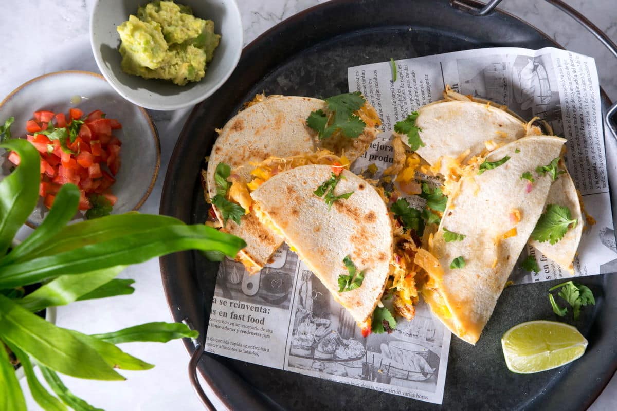 Kimchi quesadillas on dark plate with avocado and diced tomatoes on the side.