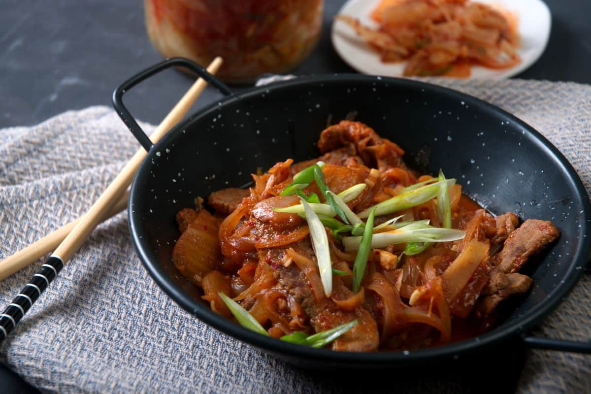 Kimchi stew in a black bowl. Chopsticks on the side and kimchi in the background.