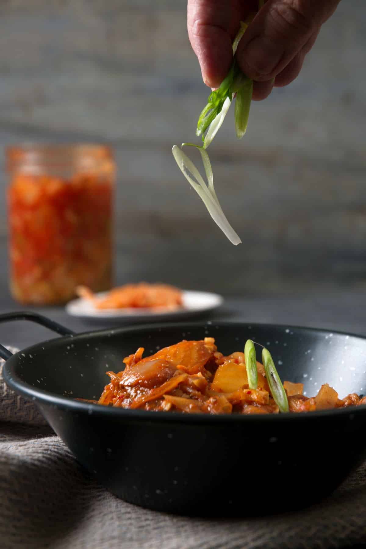 Kimchi stew in a black bowl with sliced scallions.